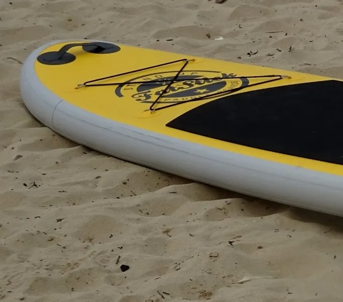 Nez d'un paddle gonflable jaune posé sur le sable